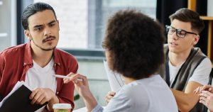 A small team in a focused discussion around a table, reviewing notes and challenging ideas during a collaborative work session.