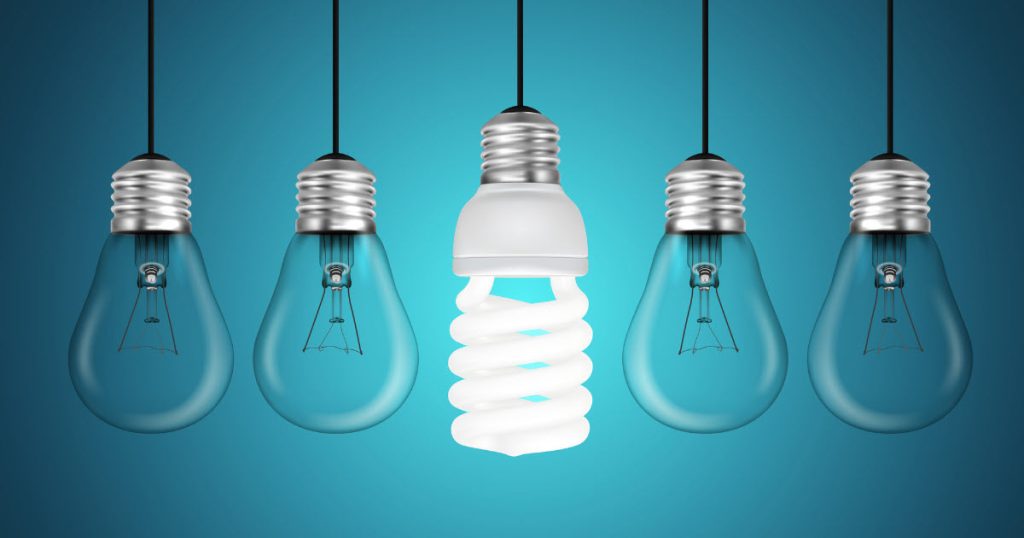 A row of hanging light bulbs, with one modern spiral bulb in the center standing out among traditional glass bulbs, symbolizing a shift away from the standard approach.